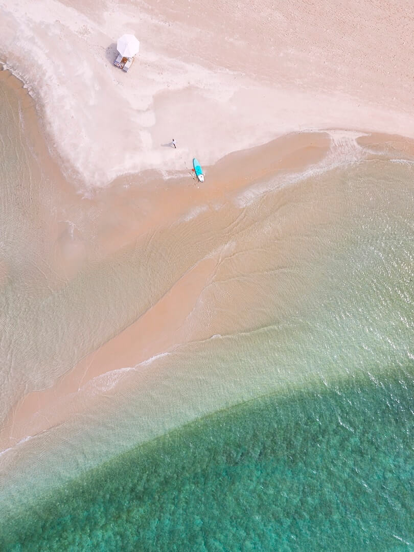 Drone shot from directly above of a paddleboard and sun loungers on a beach at Kisawa Sanctuary, Benguerra Island, photographed by Elsa Young.